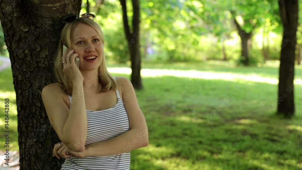 Girl is talking on the phone in the park. A woman is talking on smarfon in the background of nature. Girl is talking on the phone in the park. A woman is talking on smarfon in the background of nature.