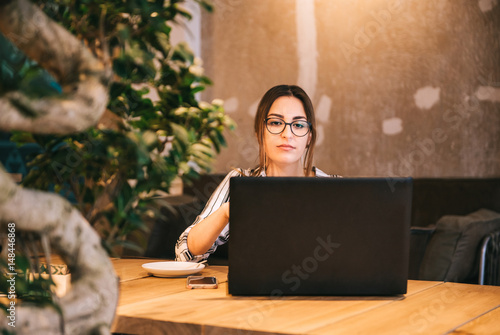 Young woman at cafe drinking coffee and using laptop