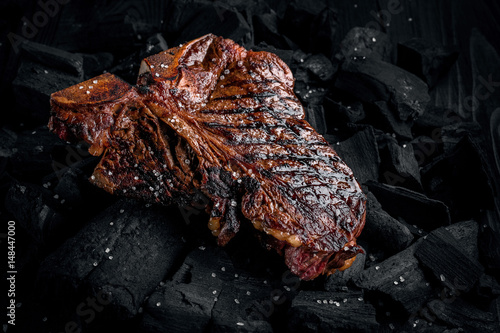 Grilling a tasty tender marinated t-bone steak on a coals. Close up view photo