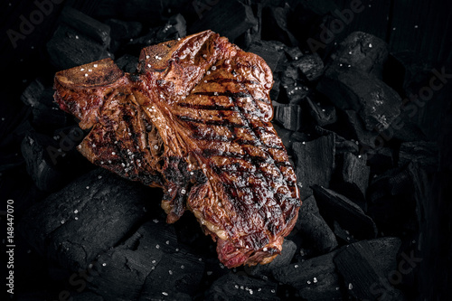 Grilling a tasty tender marinated t-bone steak on a coals. Close up view