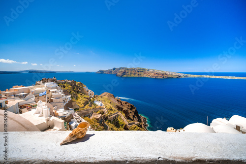 Fotografi A seashell on a ledge with Oia village and ocean background, Santorini, Greece