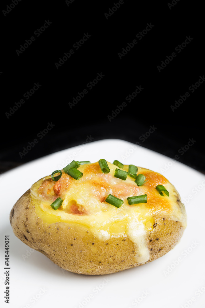 Close up of a hot baked potato topped with sour cream, bacon, green onions and cheddar cheese.
