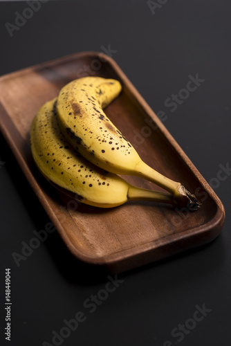 Two organic bananas in a wood sish over a black board. photo