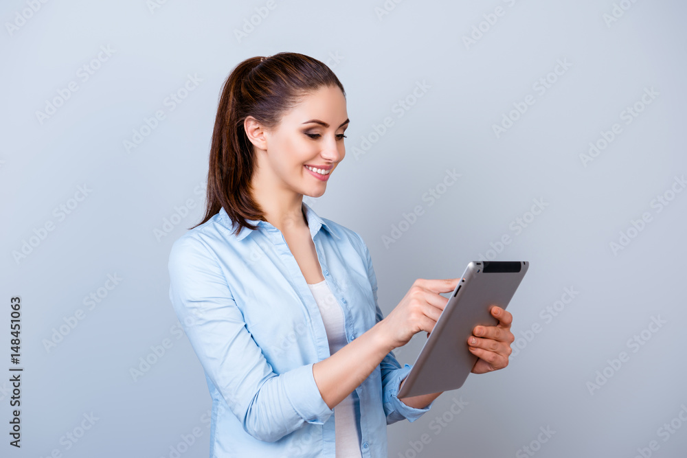 Nice-looking smiling woman in blue shirt chatting with her friends using digital tablet against gray background Nice-looking smiling woman in blue shirt chatting with her friends using digital tablet against gray background