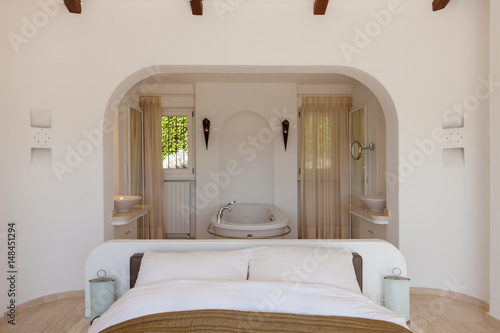 Elegant bedroom with bath tube. Front view with the bed in the foreground. No one inside the room