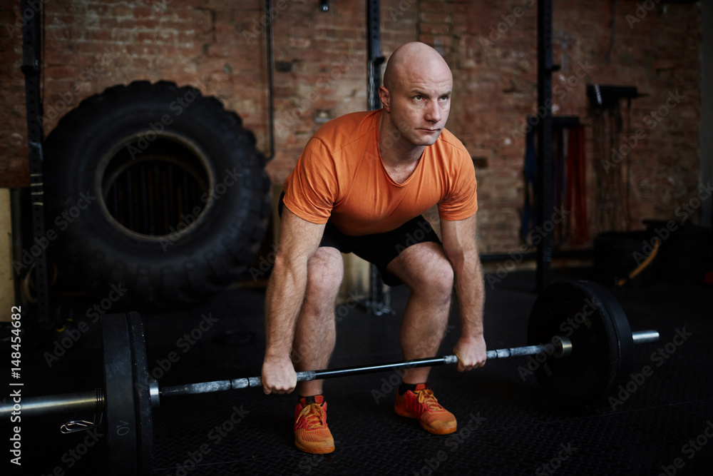 Middle-aged fit man working out with barbell in spacious gym, full-length portrait Middle-aged fit man working out with barbell in spacious gym, full-length portrait