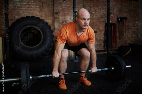 Middle-aged fit man working out with barbell in spacious gym, full-length portrait