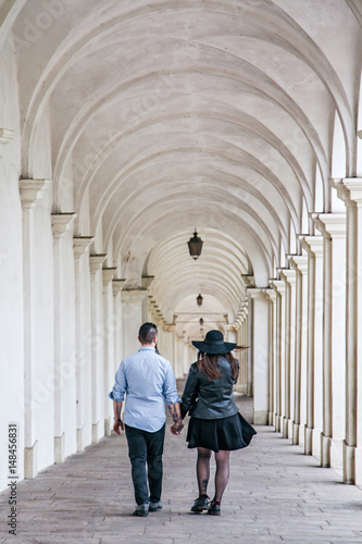 Young modern hipster couple holding hands and walking together under the arches. Deep moment of a love story with a vintage look