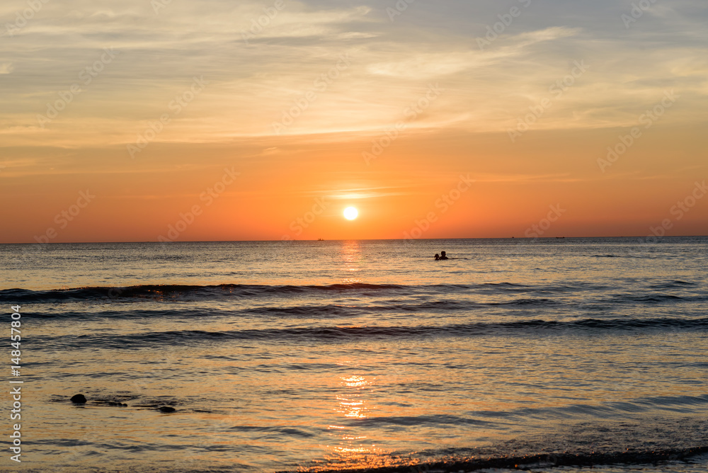 People swim and light sunset on the beach.