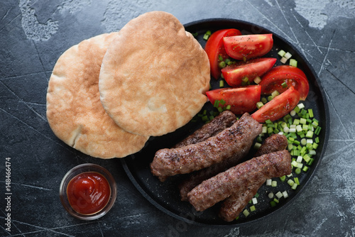 Frying pan with grilled cevapi or cevapcici sausages on a dark grey stone background, above view photo