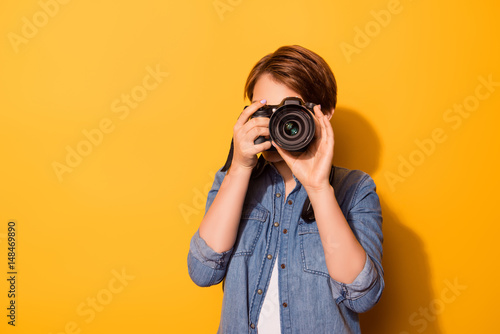 Close up photo of female photographer photographing with a camera in casual clothes on the bright yellow background photo