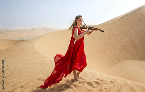 woman in a red dress playing a violin in a desert in Abu Dhabi