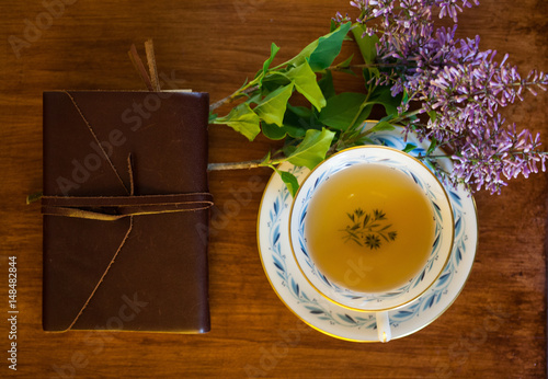 leather bound journal rests on wooden table with purple flowers and green tea in vintage teacup photo