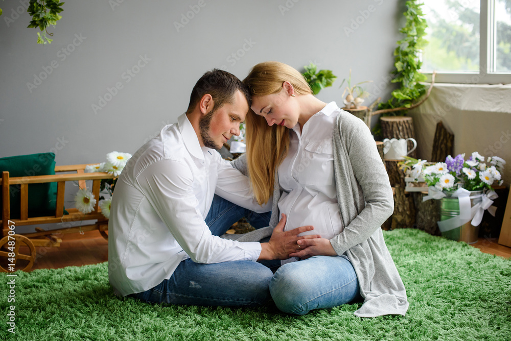 Beautiful pregnant woman and her handsome husband are smiling while spending time together. Man is listening to baby in belly