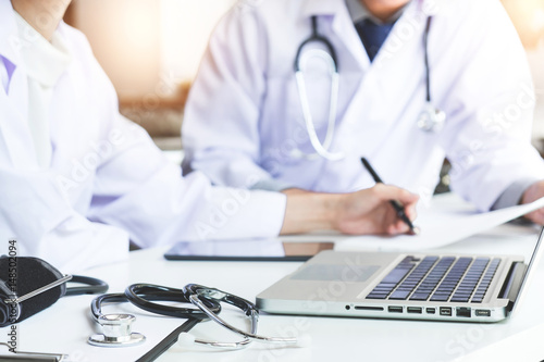 Two doctors being discussing patient history in an office pointing to a clipboard with document paper as they make a diagnosis or recommend on treatment