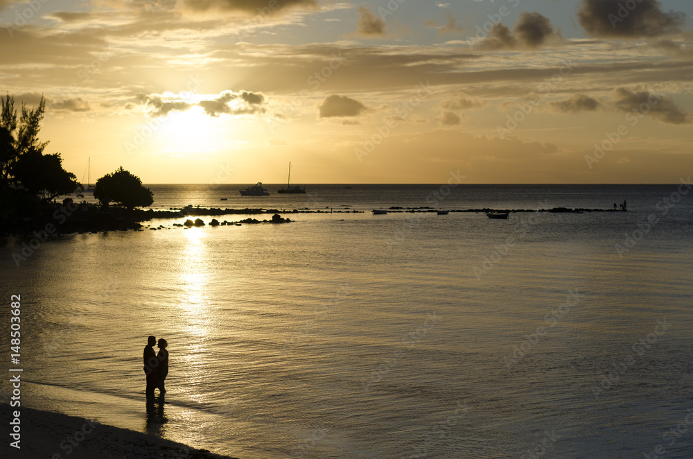 Silhouette of romantic couple on the beach at sunset with golden hour rays of light shining through epic clouds. Mauritius island, Indian Ocean.