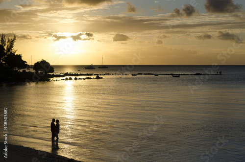 Silhouette of romantic couple on the beach at sunset with golden hour rays of light shining through epic clouds. Mauritius island, Indian Ocean.