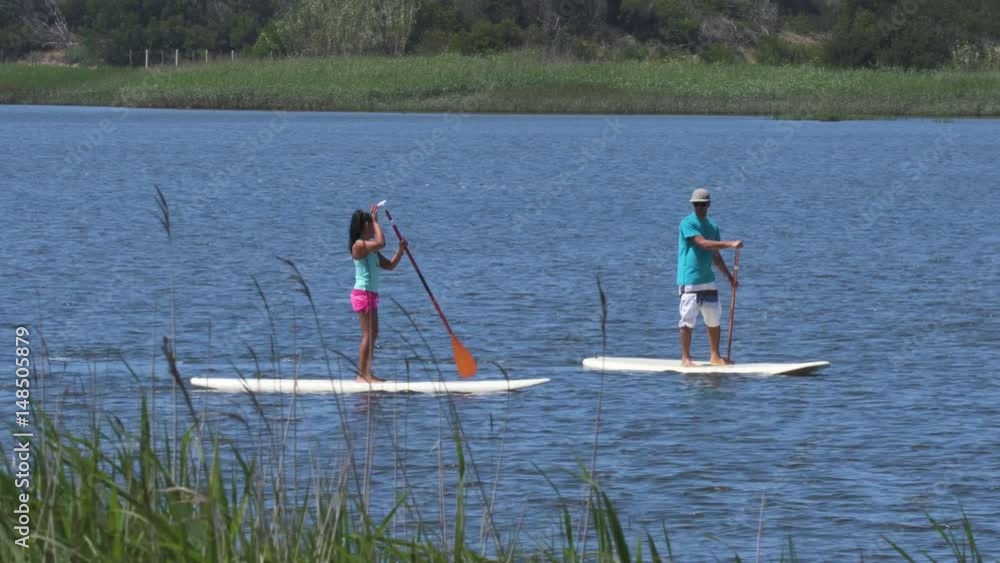 Aerial view of man and woman stand up paddleboarding on lake. Young couple are doing watersport on lake. Male and female tourists are in swimwear during summer vacation.