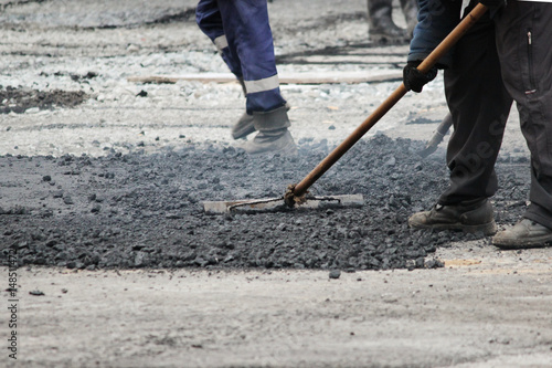 The worker is leveling the crumb of asphalt in the pit with a drag-roller before the paving with a road mini building roller.