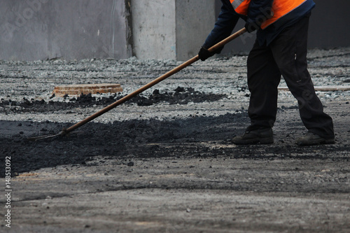 The worker is leveling the crumb of asphalt in the pit with a drag-roller before the paving with a road mini building roller.