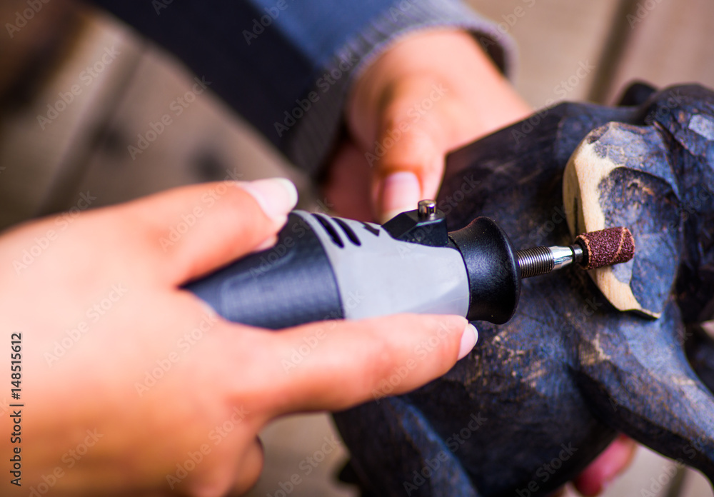 A closeup of a hardworker woman using a polisher over a wood elephant on a wooden background