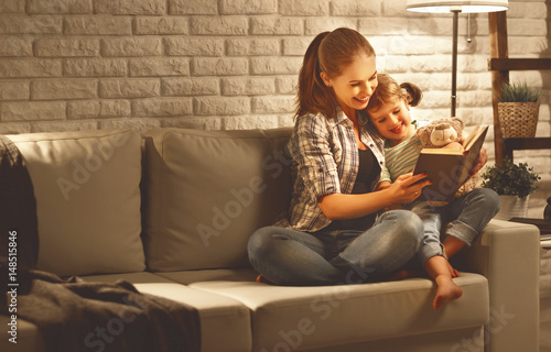 Family before going to bed mother reads to her child daughter book near a lamp in the evening