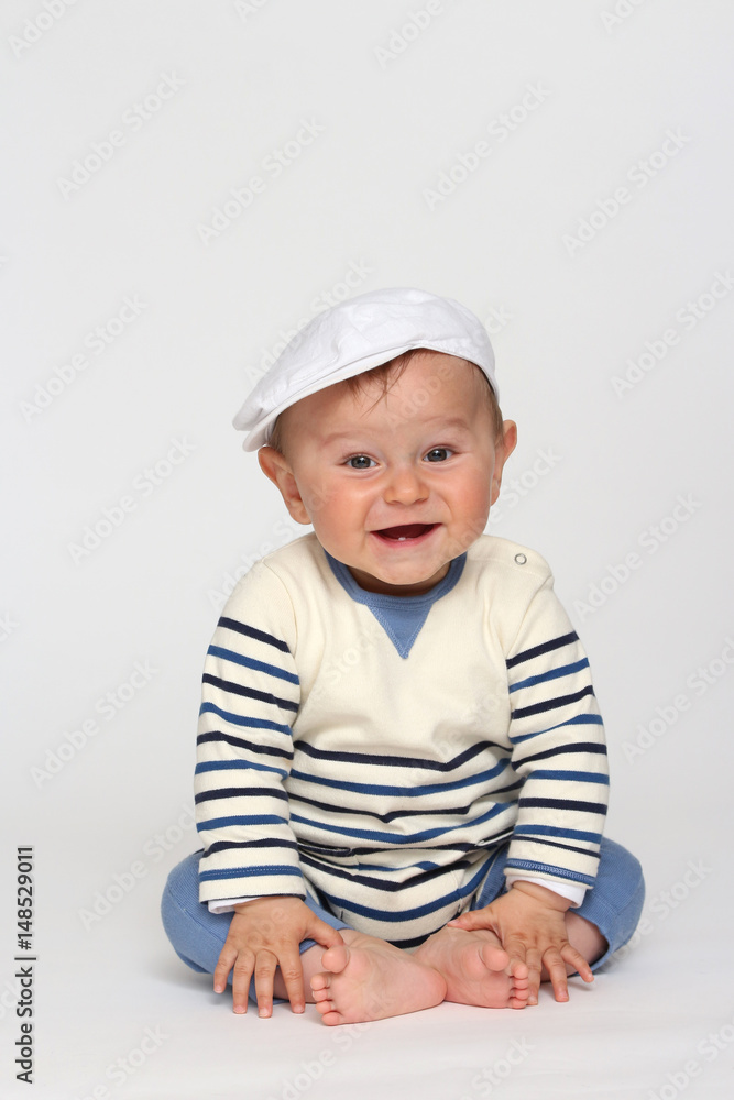 Seated baby wears a cap on a gray background Seated baby wears a cap on a gray background