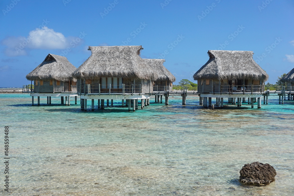 Tropical lagoon and overwater bungalows with thatched roof, atoll of Tikehau, Tuamotu, French Polynesia, south Pacific ocean
