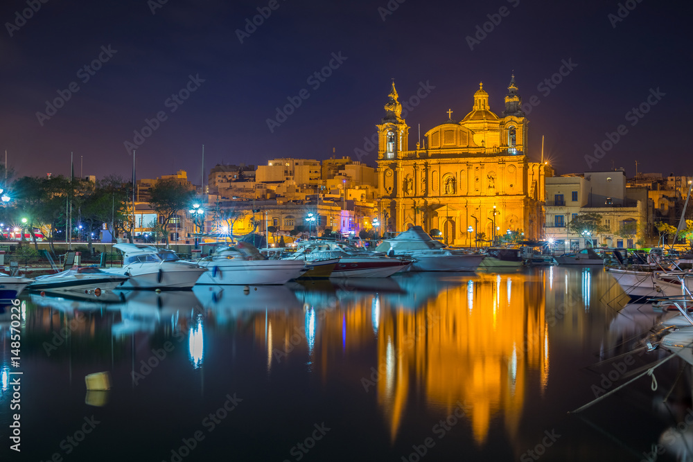 Msida, Malta - The beautiful Msida Parish Church with yachts and boats and reflection on the water by night