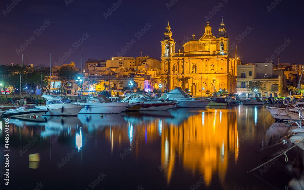 Msida, Malta - The beautiful Msida Parish Church with yachts and boats and reflection on the water by night