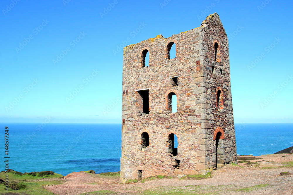 Derelict abandoned Cornish tin mine building on coast path with sea and blue sky in distance Derelict abandoned Cornish tin mine building on coast path with sea and blue sky in distance