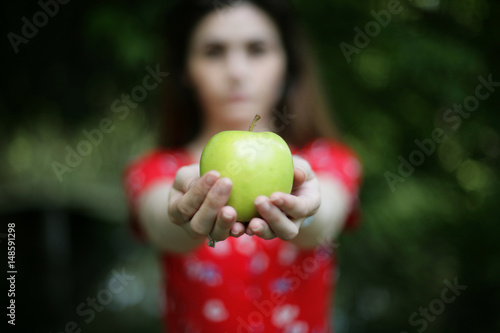 Woman hands holding a green apple; young woman offering an apple; food and generosity concept; selective focus.