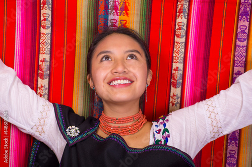 Closeup of a beautiful hispanic model wearing andean traditional clothing smiling and posing for camera, colorful fabrics background