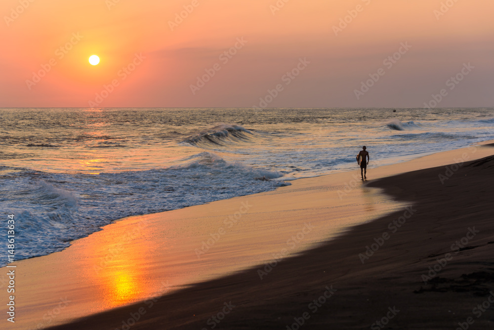 Silhouette of surfer walking on beach at sunset