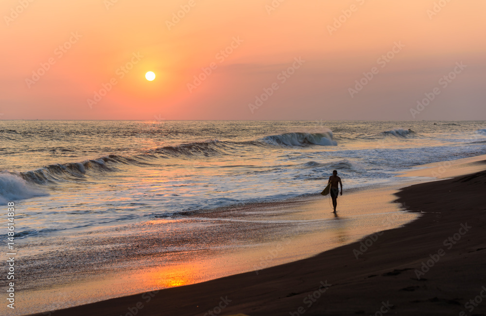 Silhouette of surfer walking on beach at sunset