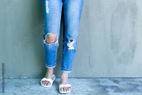 Photos Young woman fashion with ripped jeans and flip flop with concrete wall
