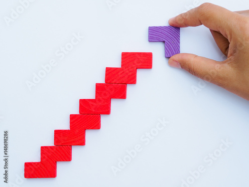 Concept of building success foundation. Women hand put difference color of puzzle wooden blocks in the shape of a staircase