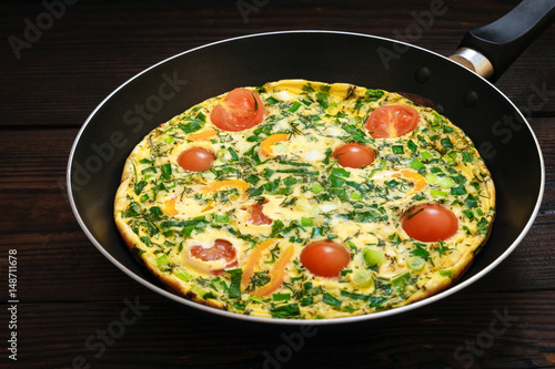 Omelette with tomato and pepper in a black frying pan on a dark wooden background