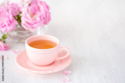 Cup of tea and bouquet of pink roses on rustic table.