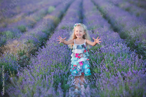 Young mother with young daughter smiling on the field of lavender .Daughter sitting on mother hands.Girl in colorful dress and mother in dark blue dress.