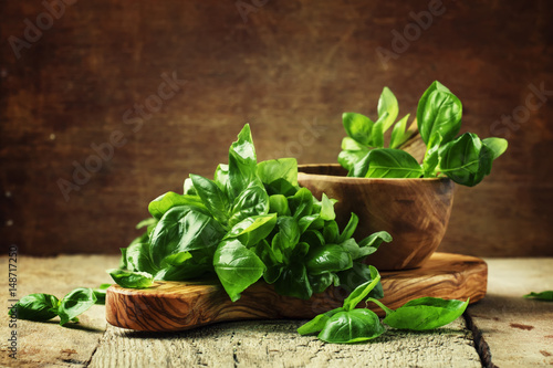 Fresh green basil in olive mortar with pestle, vintage wooden background, rustic style, selective focus