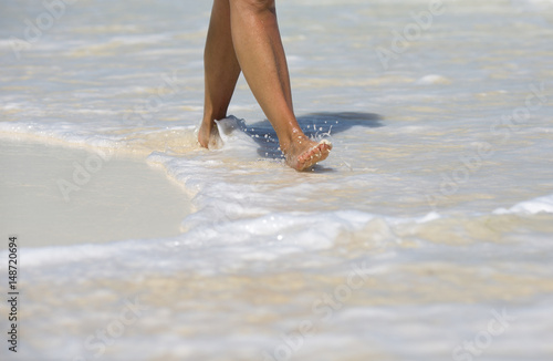 Vacation concept image. A tanned caucasian woman is walking barefoot on the beaches of the Caribbean sea. Foamy waves with white sand.
