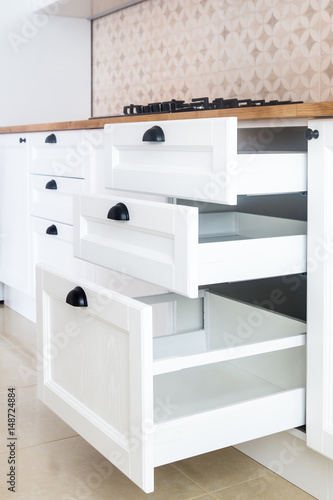 Opened kitchen drawer, kitchen in a traditional style with wooden white facade, black handles and wooden countertop 