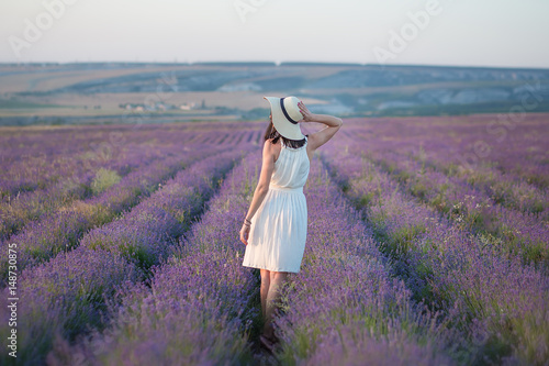 Young beautiful lady with lovely face walking on the lavender field on a weekend day in wonderful dresses and hats.