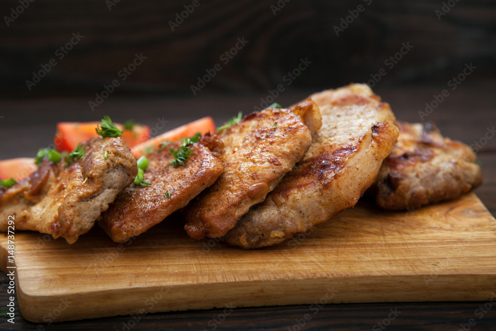 Sliced grilled pork barbecue meat on wooden cutting board over dark background Sliced grilled pork barbecue meat on wooden cutting board over dark background