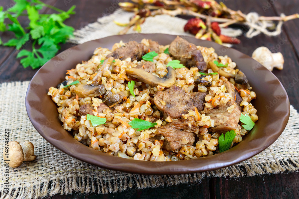 Buckwheat porridge with pieces of meat and mushrooms on a dark wooden background. Buckwheat porridge with pieces of meat and mushrooms on a dark wooden background.