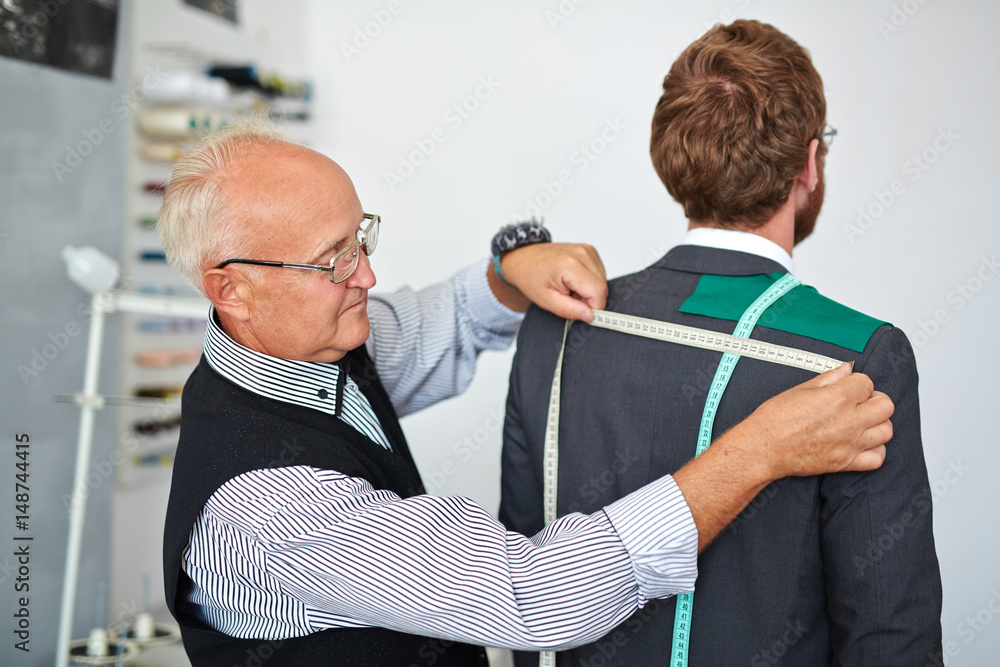 Old fashioned mature tailor taking back measurements from client in small  atelier studio to make custom classic suit with jacket Stock Photo | Adobe  Stock