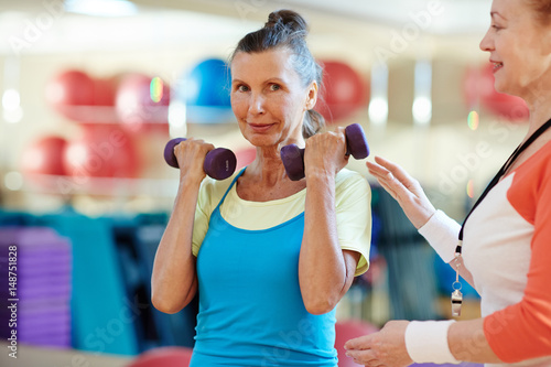 Aged woman looking at camera while exercising in gym