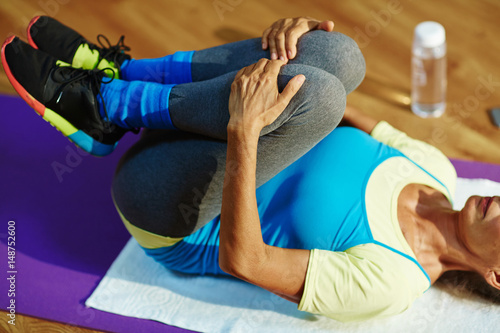 Senior female lying on mat while exercising in gym