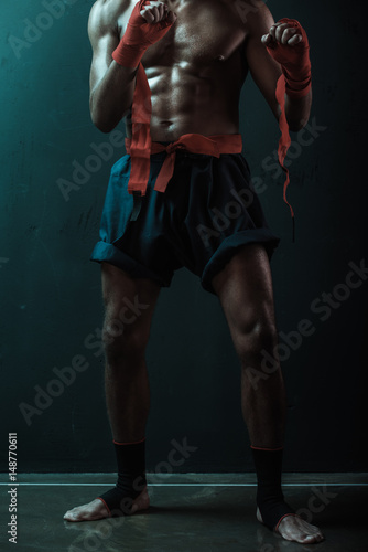 Cropped shot of shirtless and barefoot Muay thai fighter standing indoors, action sport concept